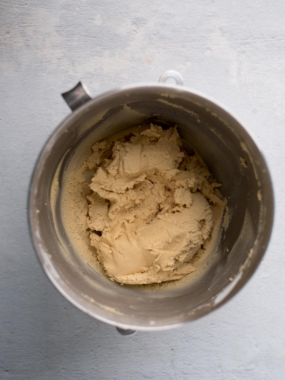 A mixing bowl filled with smooth, creamy vanilla pudding cookie dough sits on a light gray surface, viewed from above.
