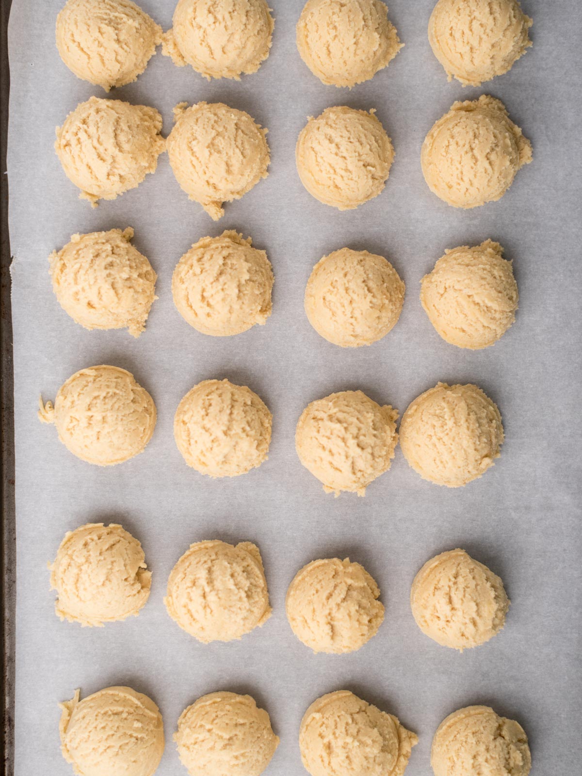 Scoops of pudding mix cookie dough are arranged neatly in rows on a parchment-lined baking sheet, ready to be baked.