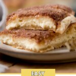 A close-up of two square slices of sopapilla cheesecake stacked on a plate. The cheesecake has a golden, flaky exterior with a cinnamon sugar topping. The background is blurred, highlighting the dessert. Text reads Easy Sopapilla Cheesecake.