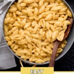 A gray pot filled with creamy stovetop macaroni and cheese, garnished with ground pepper, is on a striped towel. A wooden spoon rests inside the pot. Green beans are partially visible at the top right. The text reads Easy Stovetop Mac & Cheese.
