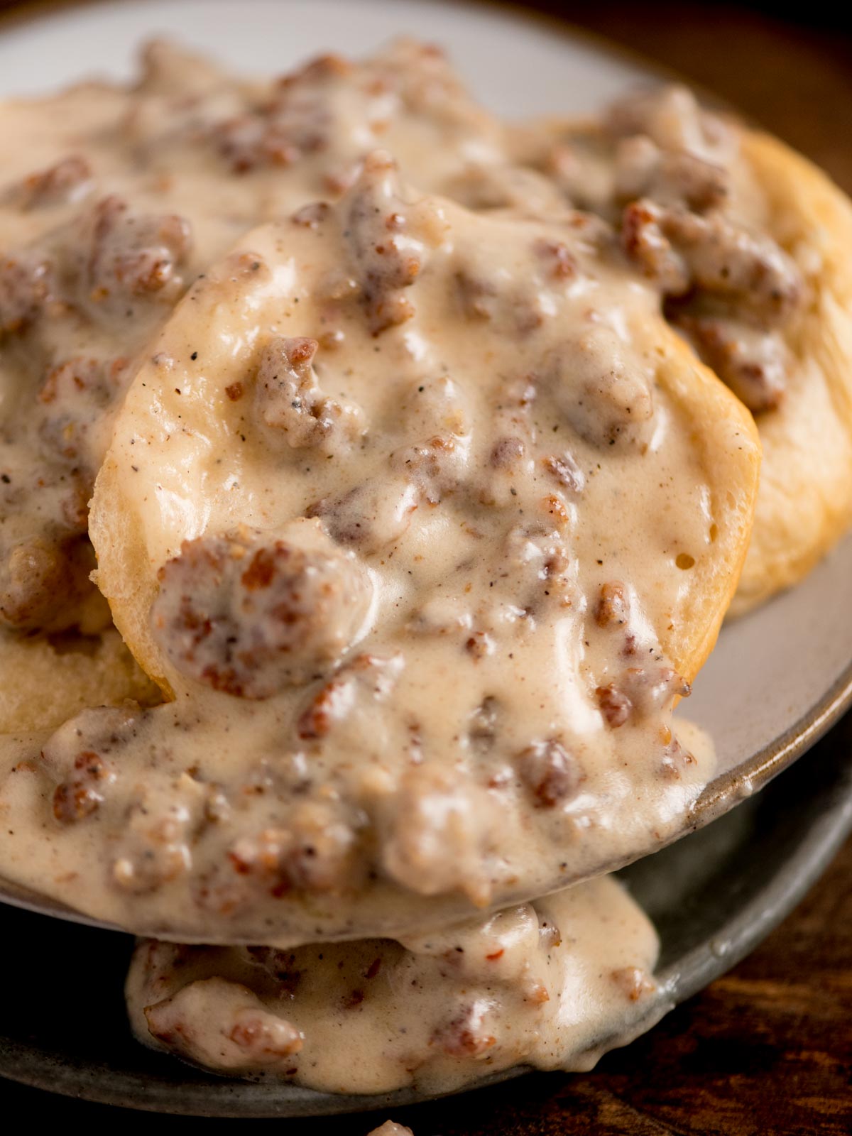 A close-up of a dish featuring biscuits topped with creamy sausage gravy. The gravy is thick and speckled with pieces of crumbled sausage, covering the golden-brown biscuits on a plate.