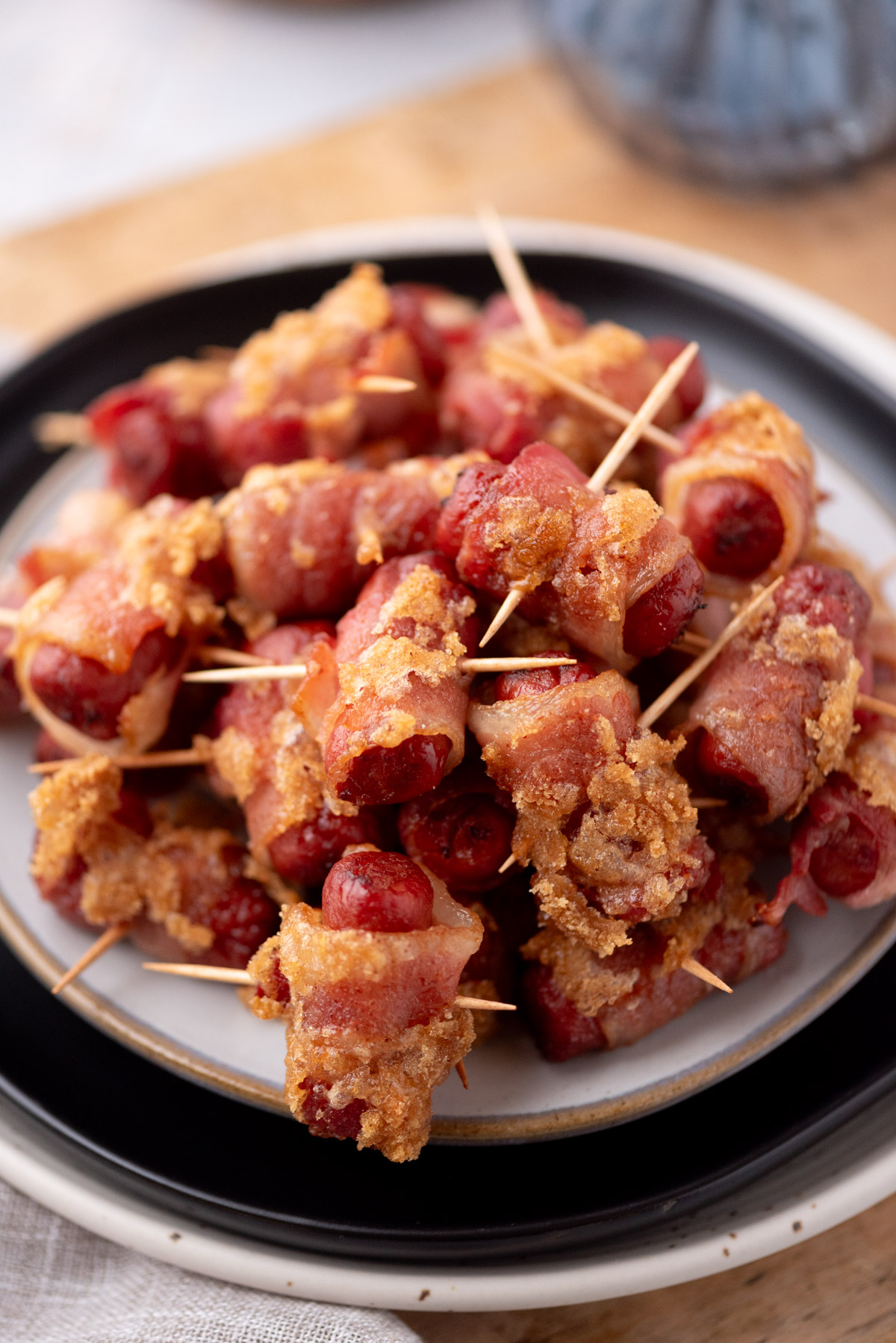 A plate stacked with bacon wrapped smokies secured with toothpicks, coated in a crispy, golden brown layer, ready to serve as appetizers.