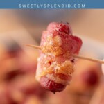 Close-up of a bacon-wrapped cocktail sausage held on a toothpick, with more bacon-wrapped smokies blurred in the background. Blue banner at the top reads bacon wrapped smokies, sweetlysplendid.com.