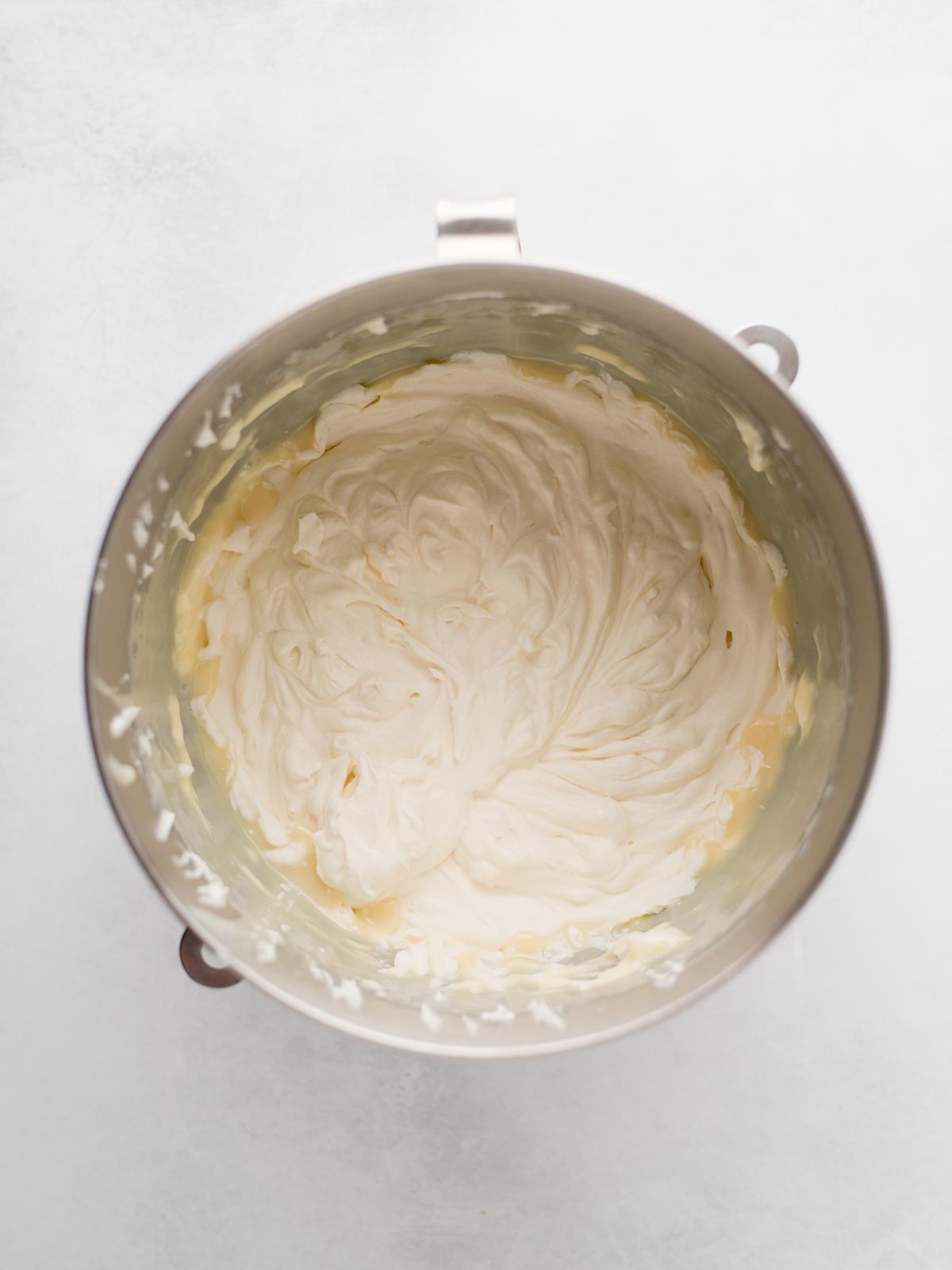 A metal mixing bowl containing light, fluffy whipped cream against a white background.