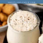 A glass jar filled with creamy Caesar dressing, topped with grated cheese and black pepper, sits on a black plate with a salad, croutons, and a text overlay that reads Easy Caesar Dressing.