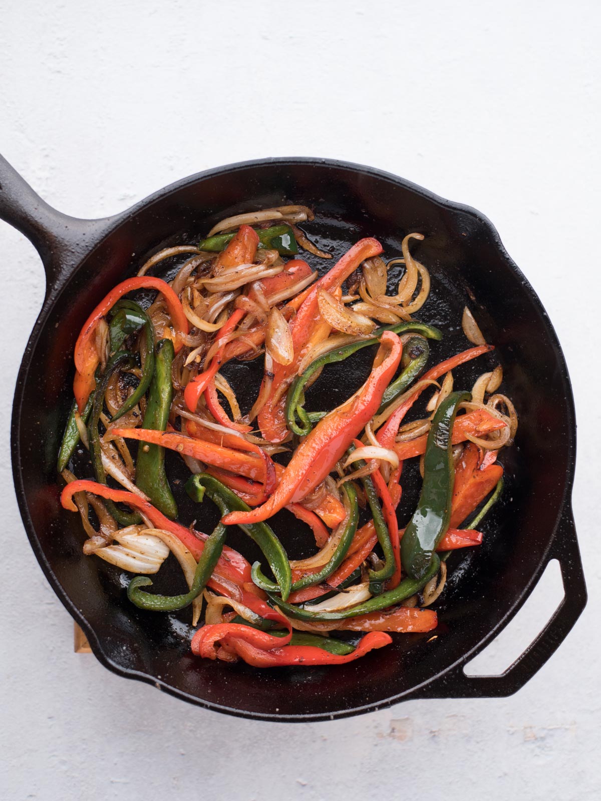 Sautéed sliced red and green bell peppers with onions in a black cast iron skillet, the perfect filling for easy chicken fajitas, viewed from above on a white background.