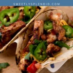 Three chicken fajita tacos topped with sliced jalapeños, shredded cheese, and diced vegetables are displayed on a wooden surface. The text chicken fajitas and sweetlysplendid.com appears above the tacos.