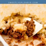 A close-up of sloppy joe casserole in a white baking dish, with a serving spoon lifting a portion to reveal the saucy ground beef filling beneath its golden, baked topping. This hearty sloppy joe casserole is perfect for family dinners.