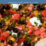 Close-up of a taco casserole topped with melted cheese, ground beef, sliced black olives, chopped tomatoes, sour cream, and green onions, with taco shells visible on the side. Text overlay reads “Taco Casserole.”.