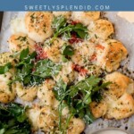 Overhead view of pull-apart cheesy bread arranged in the shape of a Christmas tree, topped with herbs and cheese, served with dipping sauces, and garnished with fresh parsley.