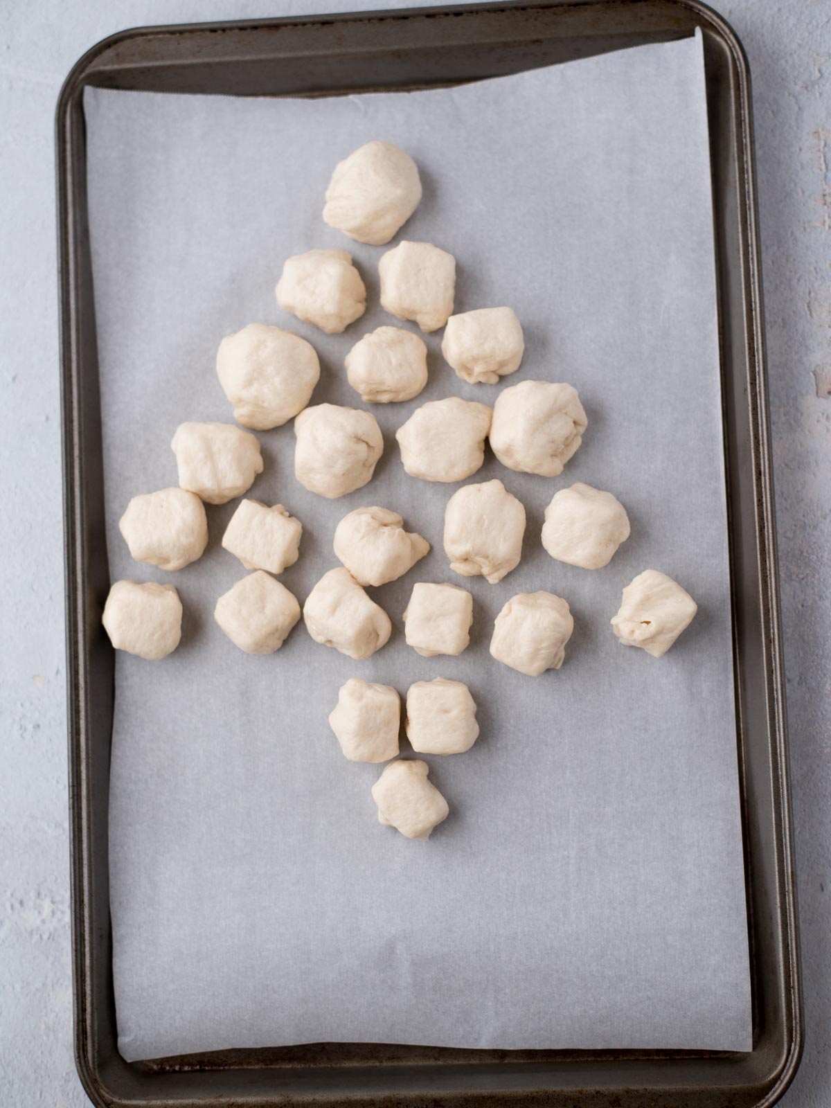 Small pieces of dough are arranged in the shape of a Christmas tree on a baking tray lined with parchment paper.