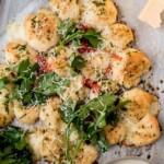 A Christmas tree-shaped pull-apart bread topped with herbs and parmesan, surrounded by fresh parsley, a bowl of dip, and marinara sauce on a parchment-lined tray.
