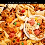 A tray and bowl filled with Halloween snack mix, including pretzels, candy corn, Bugles, Chex cereal, and colorful chocolate candies. The text reads Halloween Snack Mix, sweetlysplendid.com.