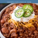 A bowl of ground beef chili with beans, topped with shredded cheddar cheese, sour cream, sliced jalapeños, and cracked black pepper, with a text overlay reading ground beef chili with beans.