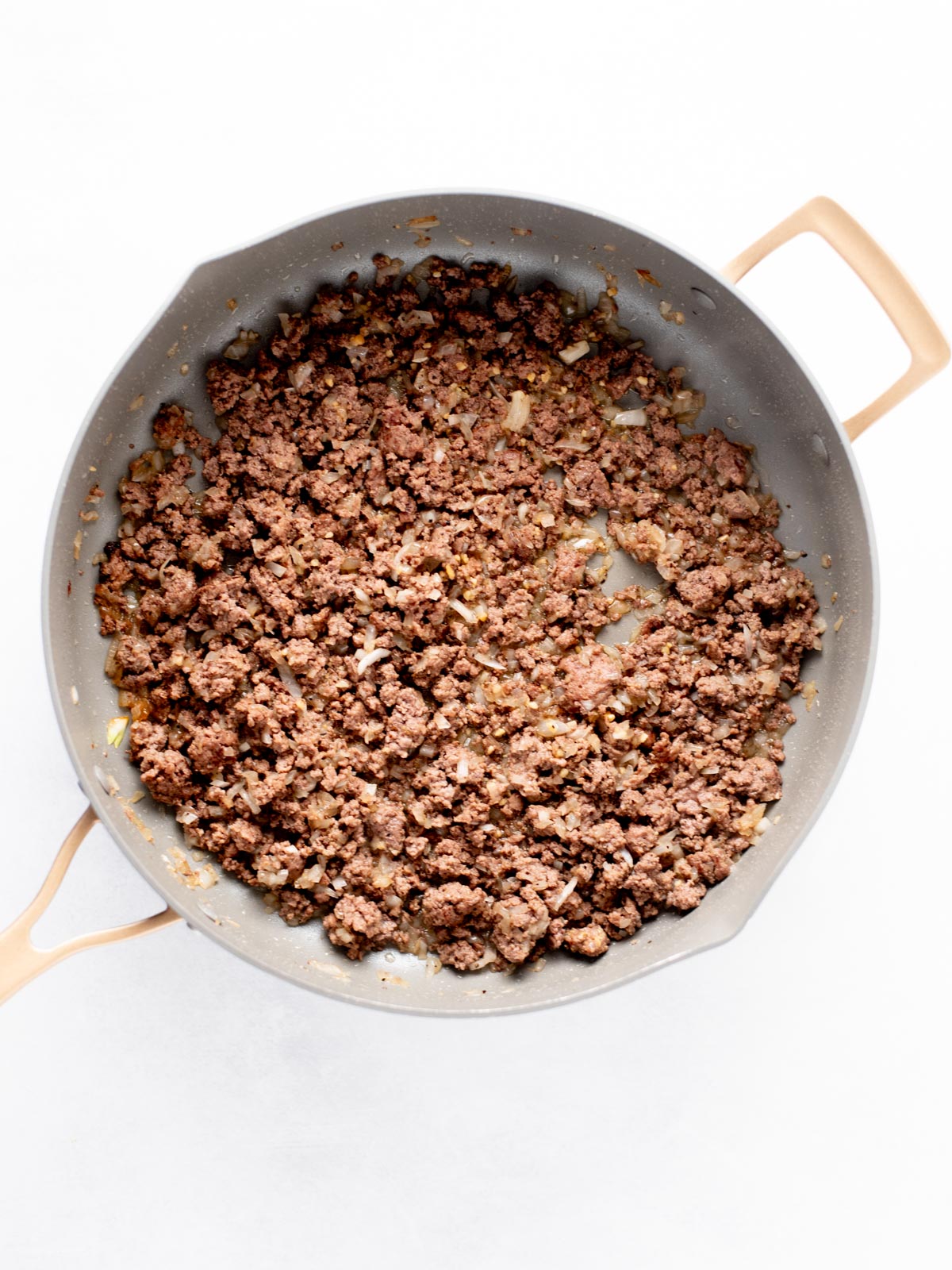 A frying pan filled with cooked ground beef and small pieces of onion, viewed from above on a white background.