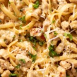 A skillet filled with creamy chicken Alfredo pasta, topped with grated cheese and fresh chopped parsley. Text at the top reads, one pot creamy chicken alfredo and sweetlysplendid.com.