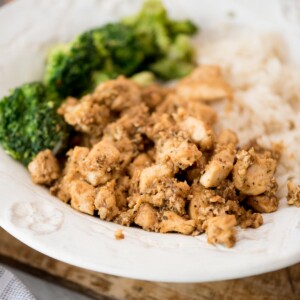 A plate of diced, seasoned chicken served with steamed broccoli and white rice on a white dish.