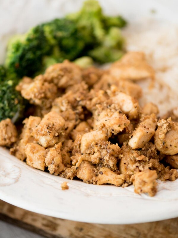 A plate of diced, seasoned chicken served with steamed broccoli and white rice on a white dish.
