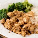 A plate of garlic brown sugar chicken served with white rice and steamed broccoli sits on a wooden surface, with a sweetlysplendid.com label and recipe title displayed at the top.