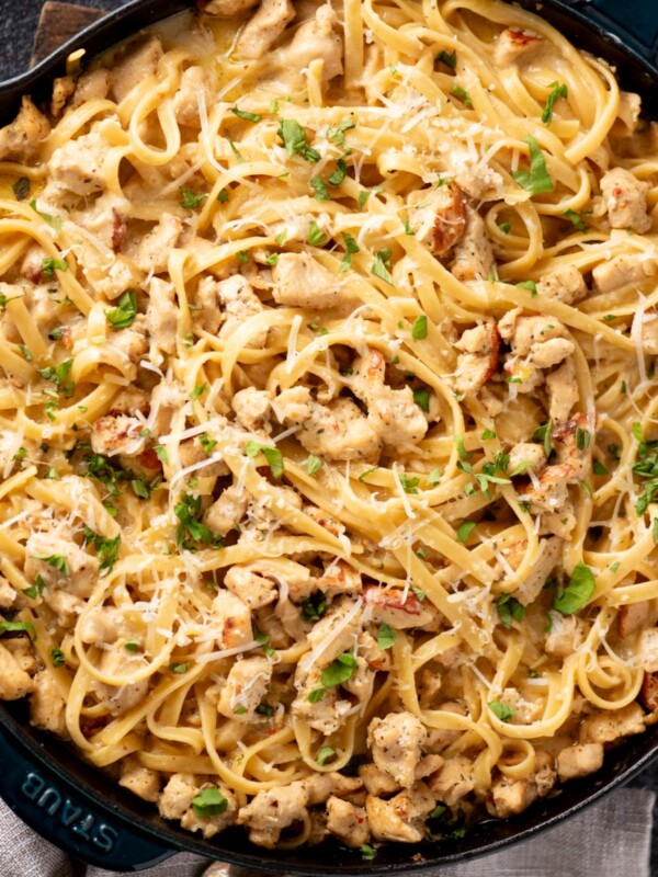 A skillet filled with creamy chicken pasta, topped with chopped herbs and grated cheese, featuring linguine noodles and pieces of cooked chicken.