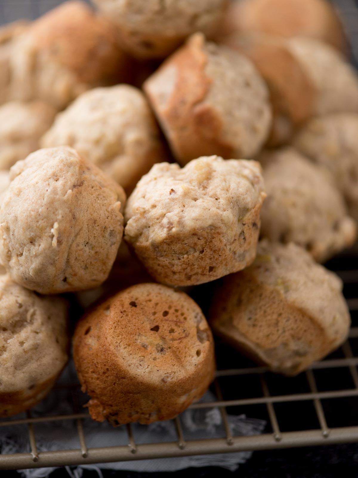 A close-up of freshly baked mini muffins with a light golden-brown color, stacked on a cooling rack.