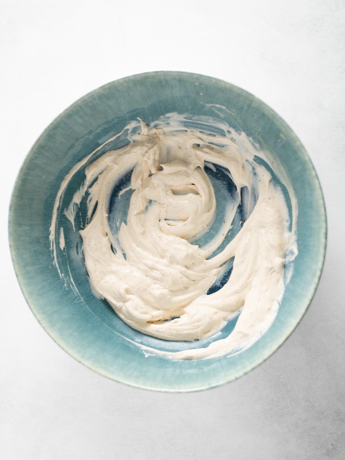 A blue bowl containing a creamy white mixture, swirled around the sides, set on a light-colored surface.