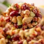A close-up of a spoonful of mixed bean salad with kidney beans, white beans, chickpeas, chopped vegetables, and herbs. Text at the top reads the best bean salad recipe with sweetlysplendid.com below.