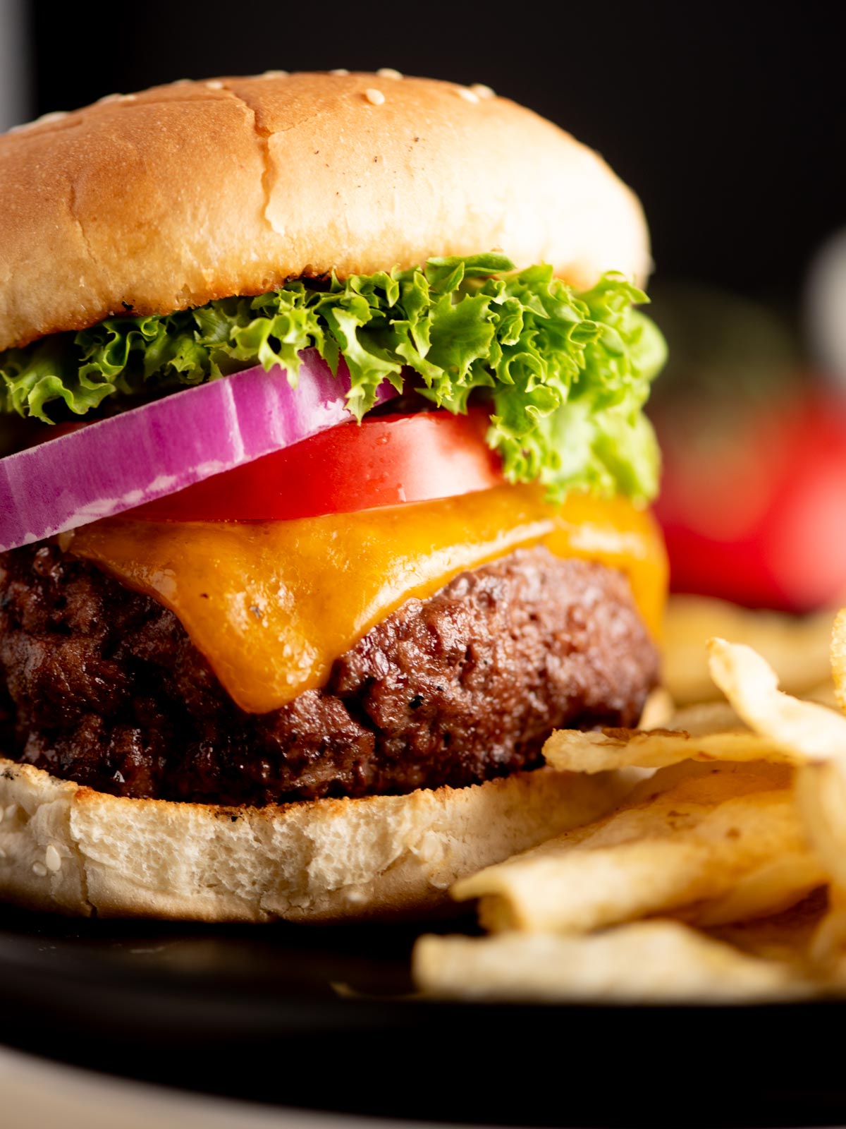 A close-up of a cheeseburger with lettuce, tomato, red onion, cheddar cheese, and a beef patty on a sesame bun, served with a side of French fries.