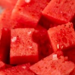 Close-up of cubed watermelon sprinkled with seasoning. A banner at the top reads, summer time watermelon snack, with the website sweetlysplendid.com below it.