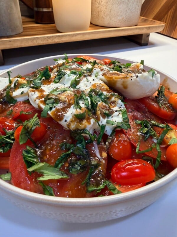 A bowl of caprese salad with sliced tomatoes, mozzarella, fresh basil, and balsamic glaze, set on a counter.