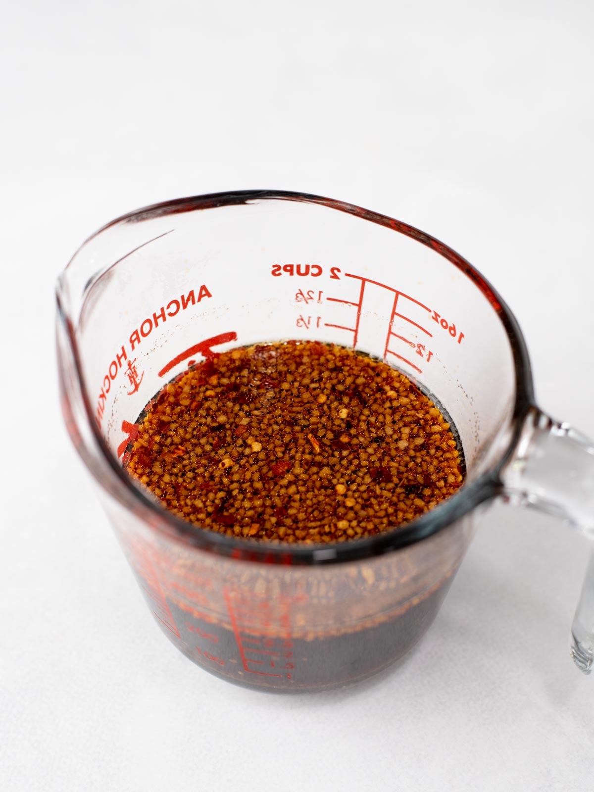A glass measuring cup filled with a dark liquid and visible minced garlic or spices, placed on a white surface.
