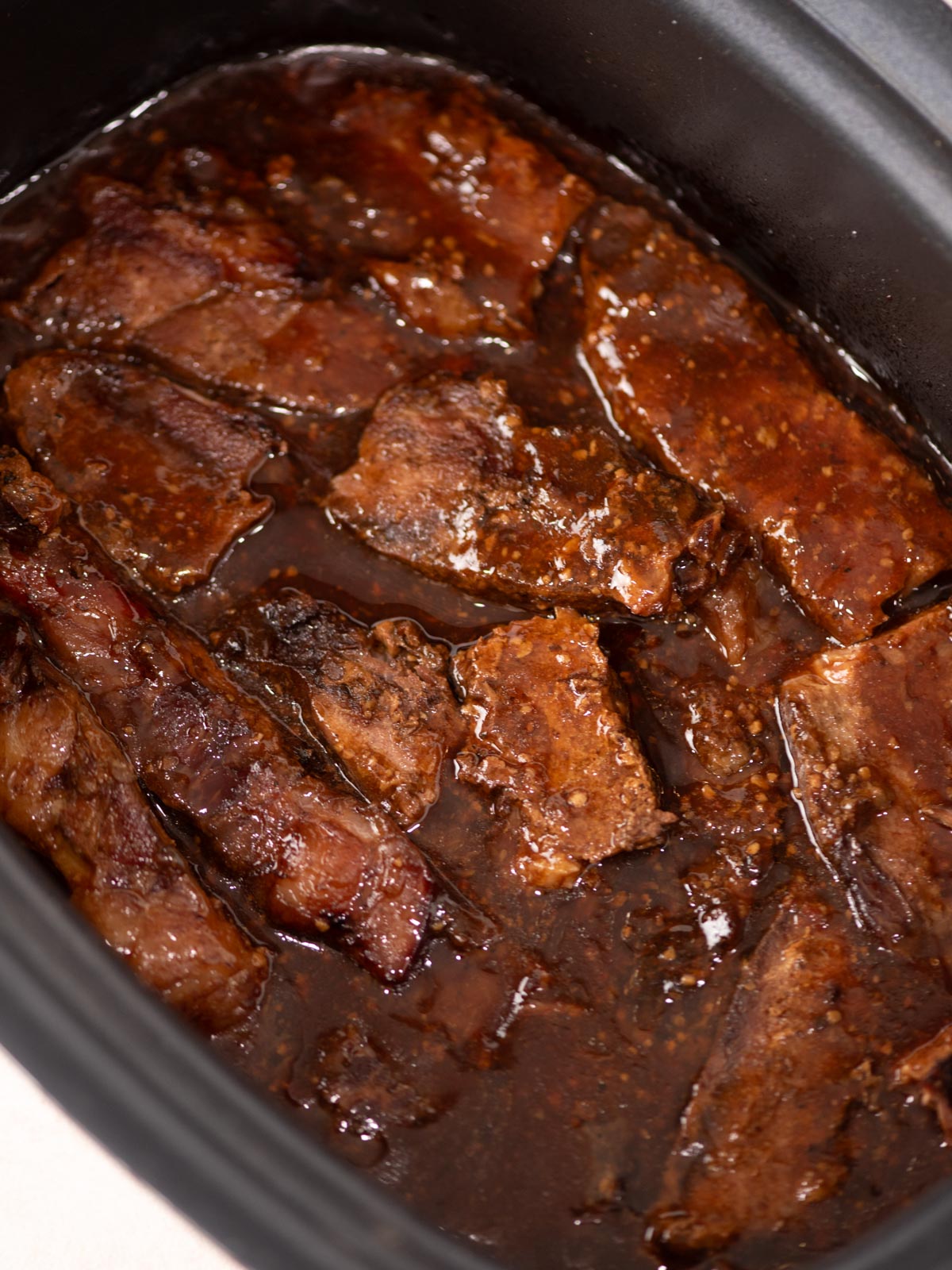 Slices of beef brisket cooked in a rich, dark brown sauce, shown inside a slow cooker. The meat appears tender and juicy, coated with the thick sauce.