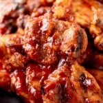 A plate of grilled BBQ chicken thighs covered in sauce, with a close-up view showing charred edges. A text overlay at the top reads grilled bbq chicken thighs and sweetlysplendid.com.