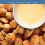 A bowl of cheese dip sits on top of a pile of golden-brown pretzel bites sprinkled with salt, arranged on parchment paper. The text above reads pretzel bites and sweetlysplendid.com..