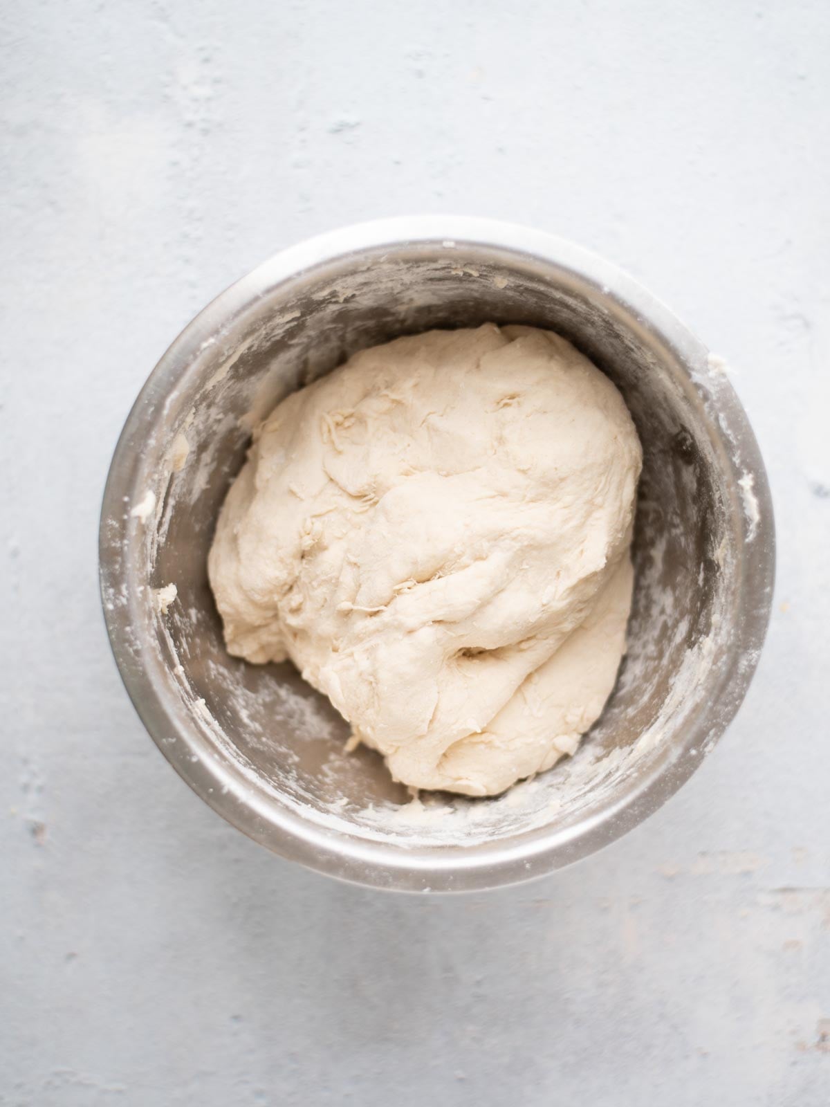 A ball of raw dough rests in a metal mixing bowl on a light-colored surface.