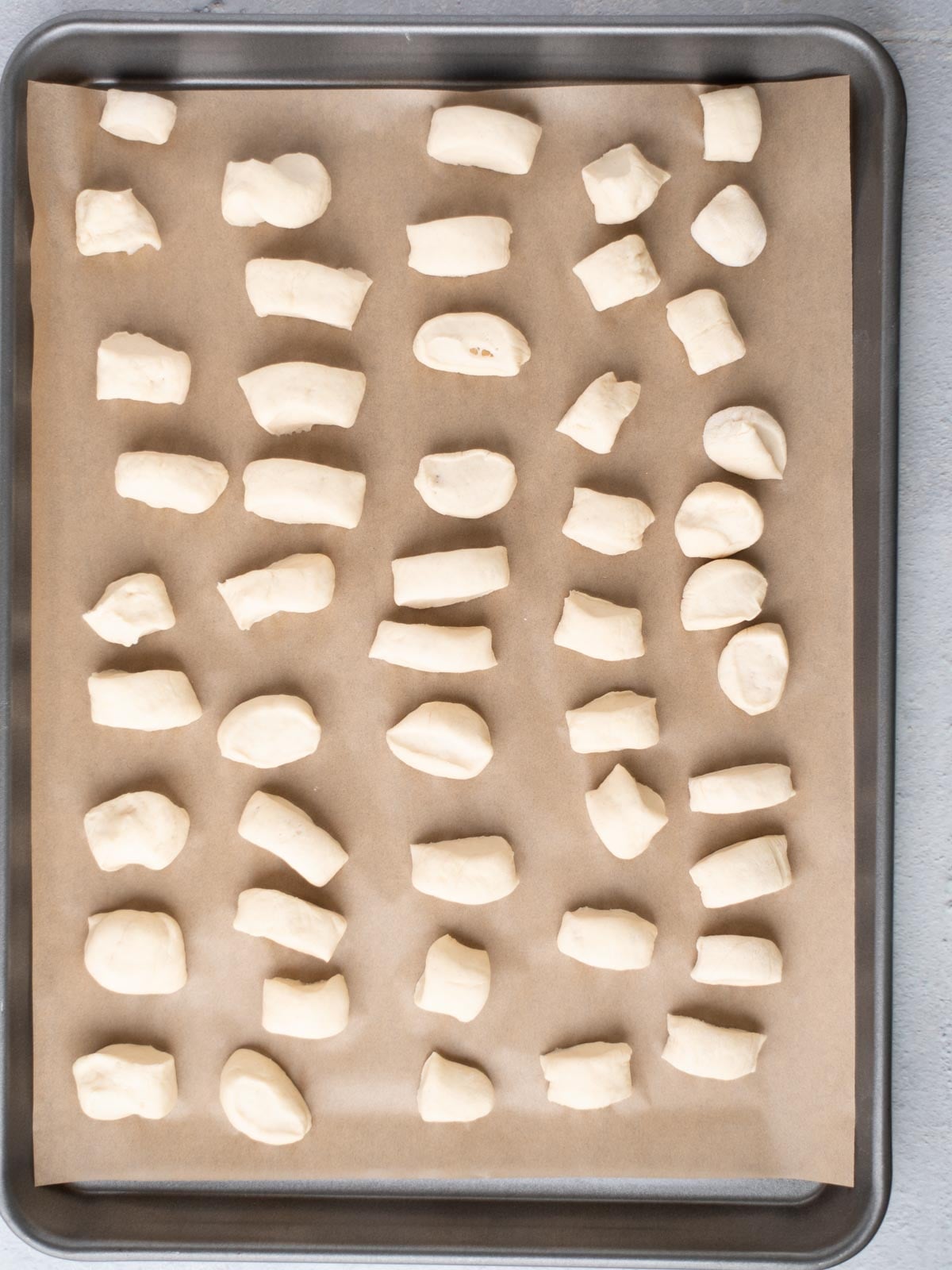 A baking tray lined with parchment paper, holding evenly spaced small pieces of uncooked dough arranged in rows, ready for baking.