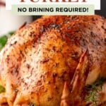 A roasted turkey seasoned with herbs on a wooden cutting board, with text overlay reading Oven Roasted Turkey: No brining required!.