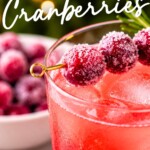 A cocktail with ice and a garnish of sugared cranberries on a skewer, with a bowl of cranberries in the background and the text SUGARED Cranberries overlaid.