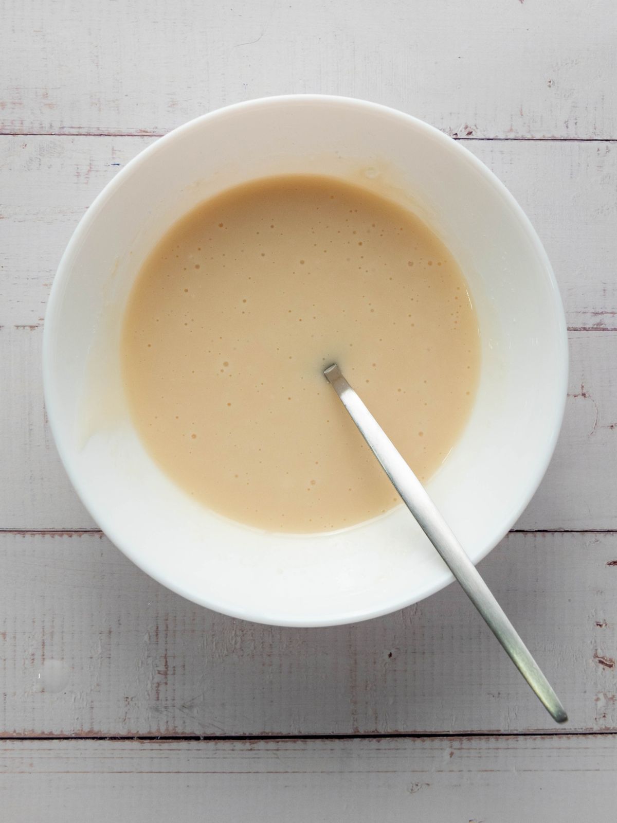 A white bowl filled with light-colored cake batter and a metal spoon.