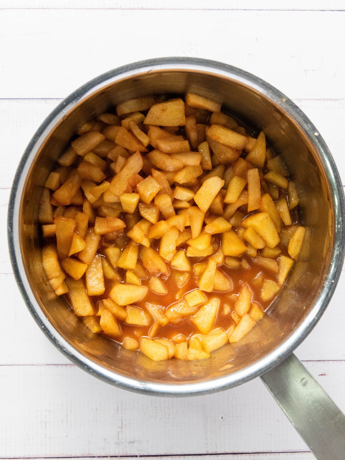 A saucepan filled with diced apples cooked in a cinnamon-spiced sauce.