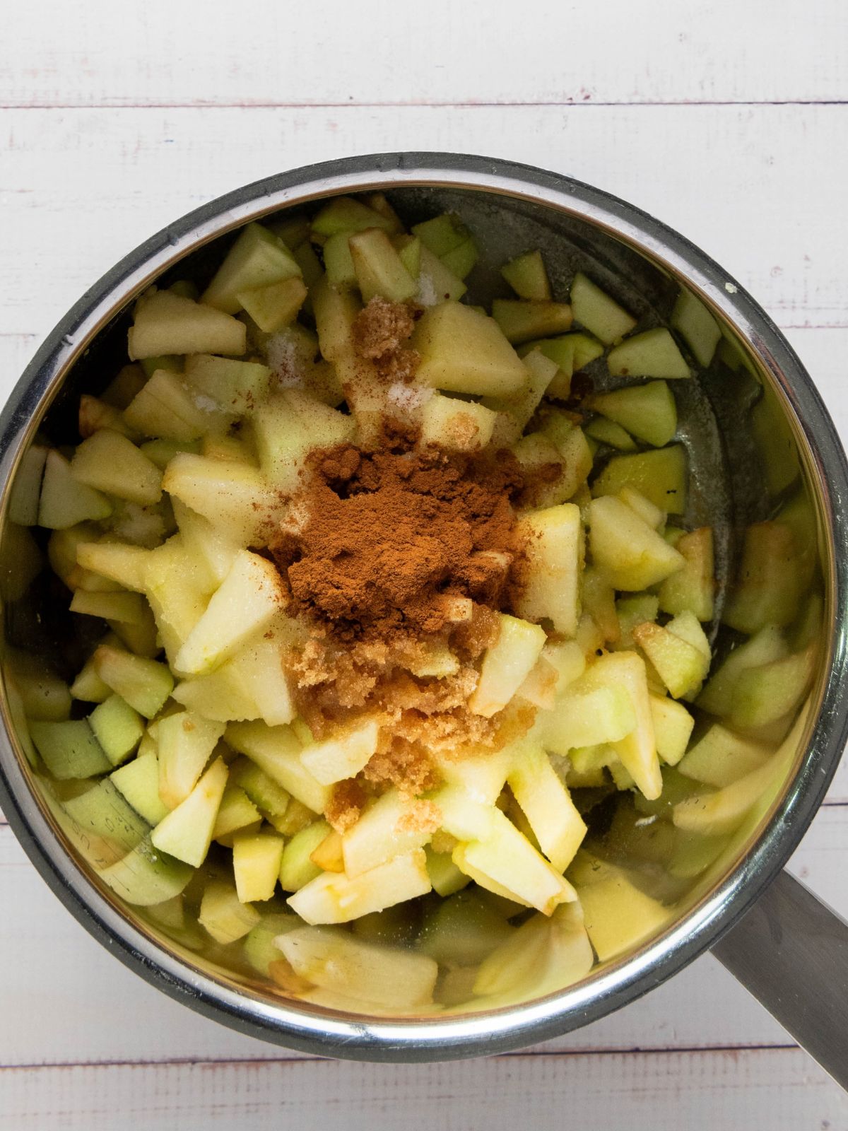 A metal pot filled with chopped apples, topped with a mound of brown sugar and cinnamon.