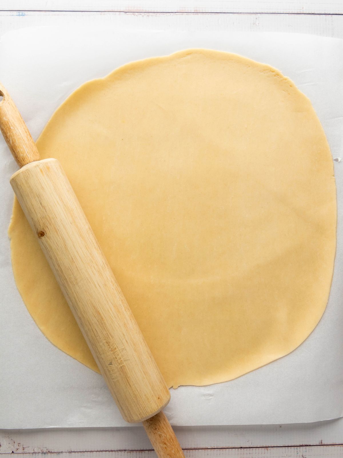 A wooden rolling pin resting on a sheet of rolled-out pie dough.