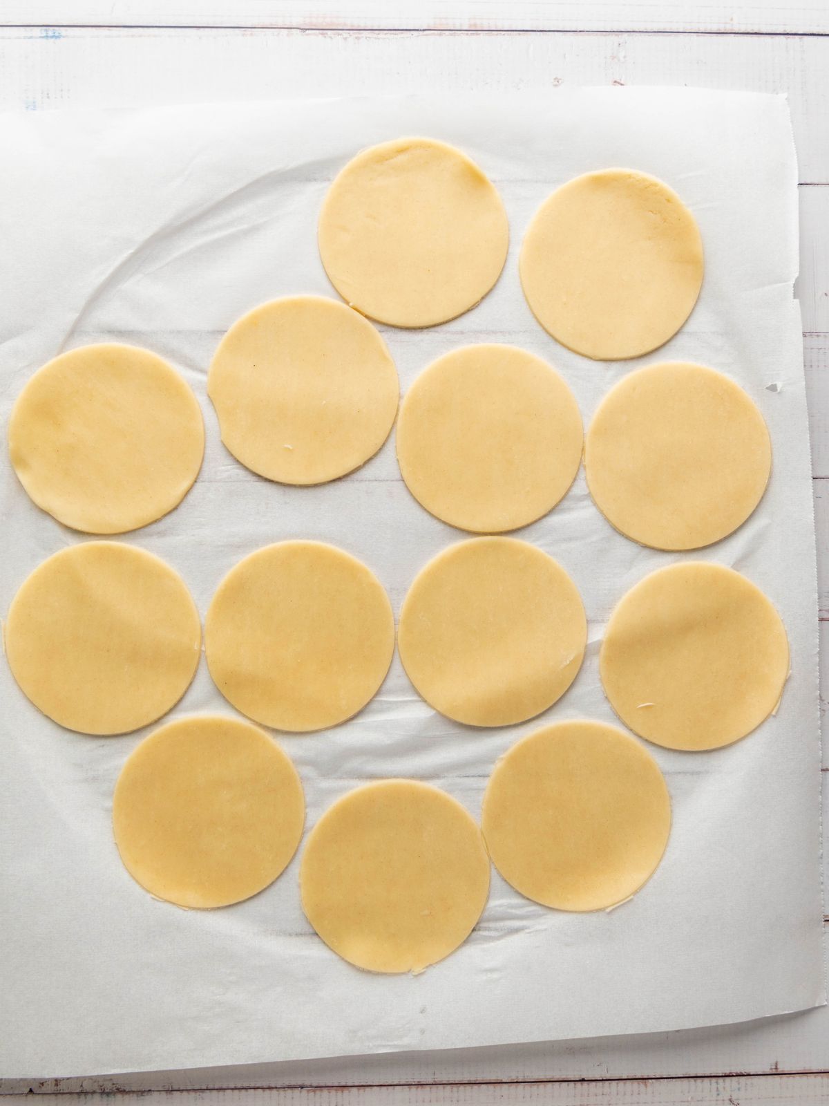 Twelve circular cutouts of raw dough arranged on a sheet of parchment paper.