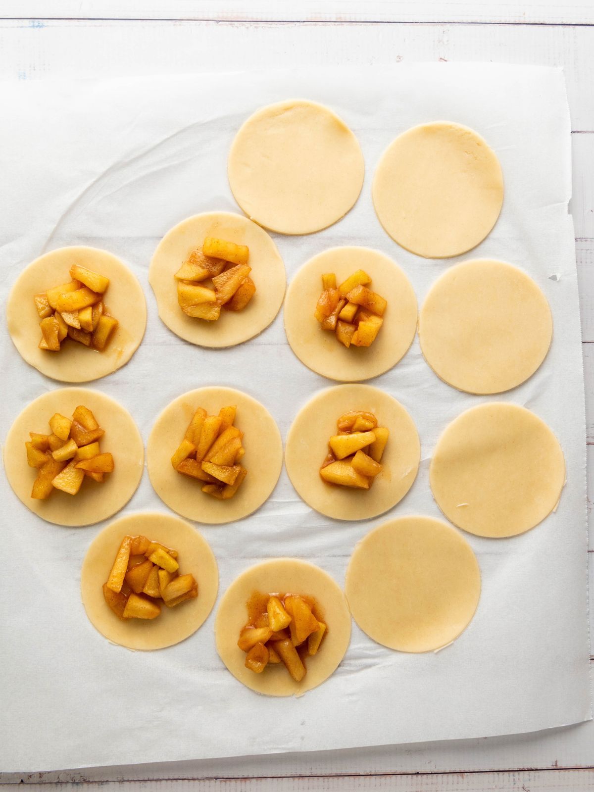 Circular dough cutouts on parchment paper, some topped with mounds of cooked, sliced apples.
