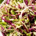 A bowl of vibrant cilantro lime slaw with shredded green and purple cabbage, perfect for tacos. A label at the top reads cilantro lime slaw for tacos with sweetlysplendid.com underneath.