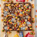 A square brownie topped with candy corn, pumpkin-shaped candies, chocolate bars, and colorful sprinkles, sitting on a wooden board.