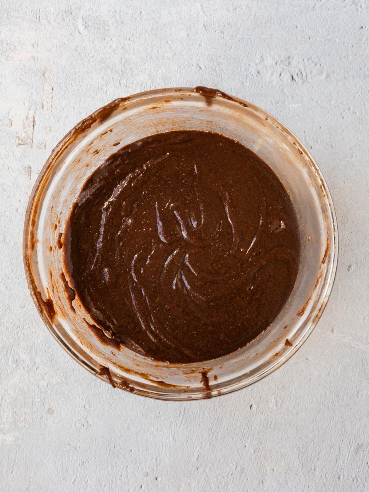 A glass bowl filled with smooth, dark chocolate cake batter.
