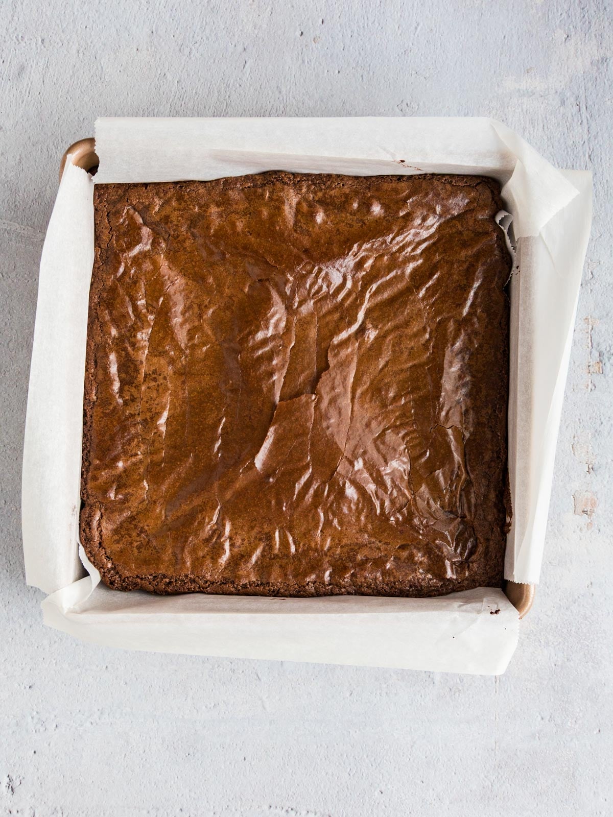 A square chocolate brownie baked in a parchment-lined metal pan.