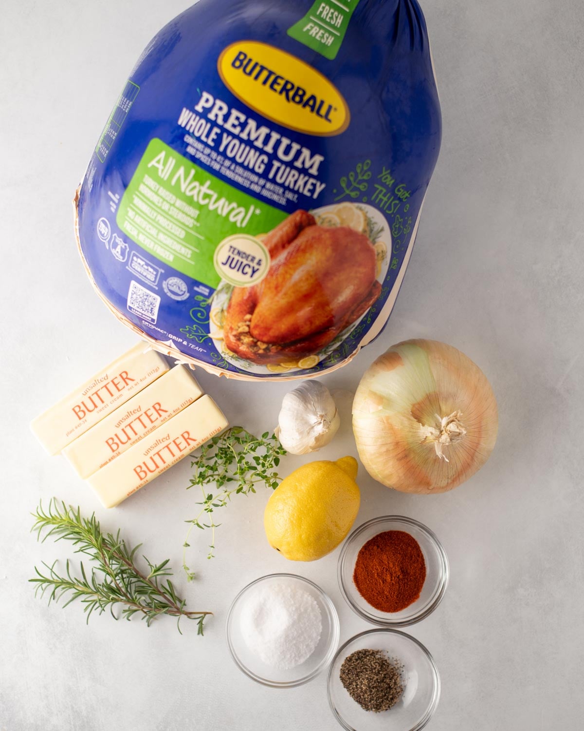 A Butterball whole young turkey with ingredients for cooking including three sticks of butter, a whole onion, a head of garlic, a lemon, fresh rosemary and thyme, salt, pepper, and paprika.
