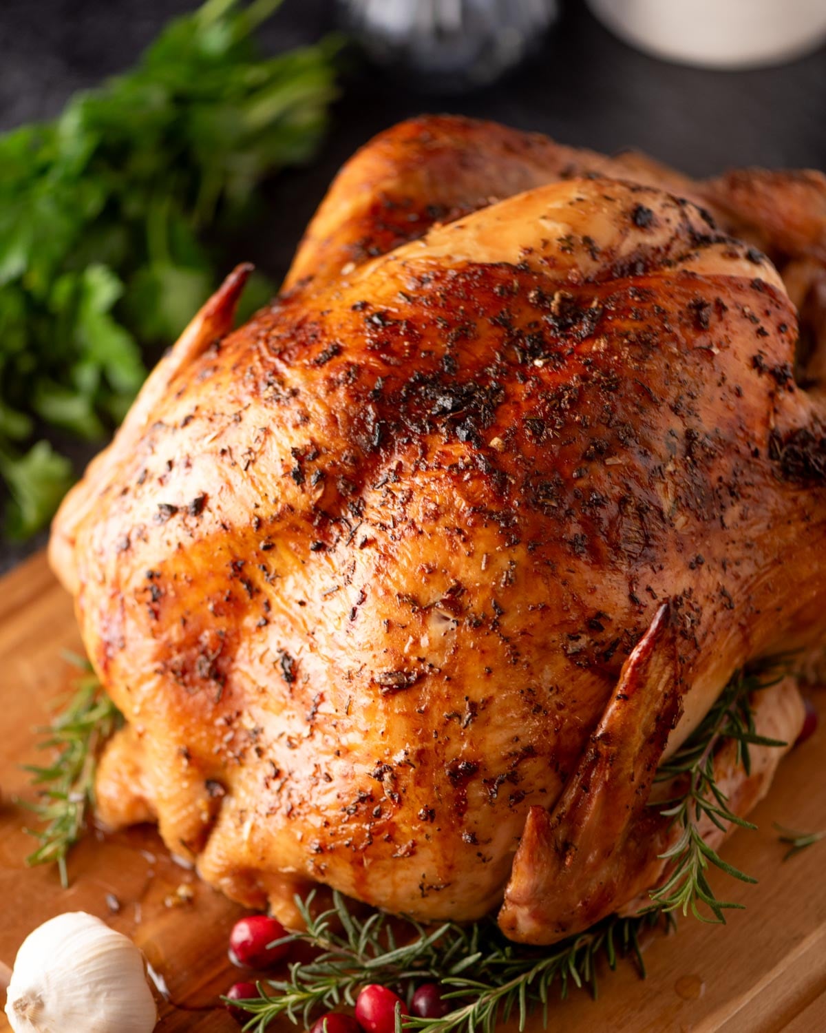 A whole roasted chicken garnished with fresh rosemary sprigs, cranberries, and a head of garlic on a wooden board.